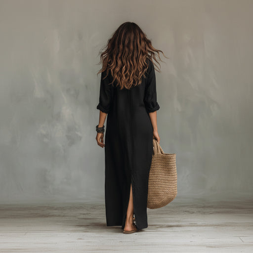 Person wearing a black dress holding a woven bag against a gray wall.