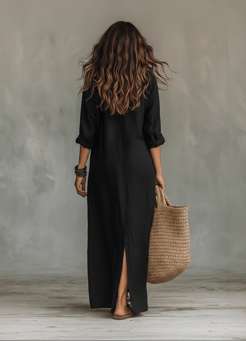 Person wearing a black dress holding a woven bag against a gray wall.