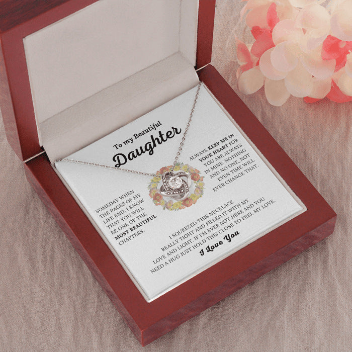 Necklace in a wooden box with a message card for a daughter, on a soft fabric background.