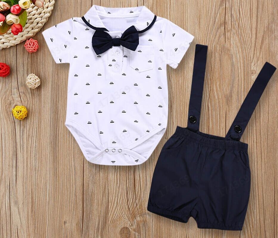 Baby outfit with white romper and black suspenders on a wooden surface