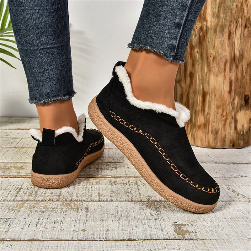 Black slippers with white fur trim worn by a person on a wooden floor.