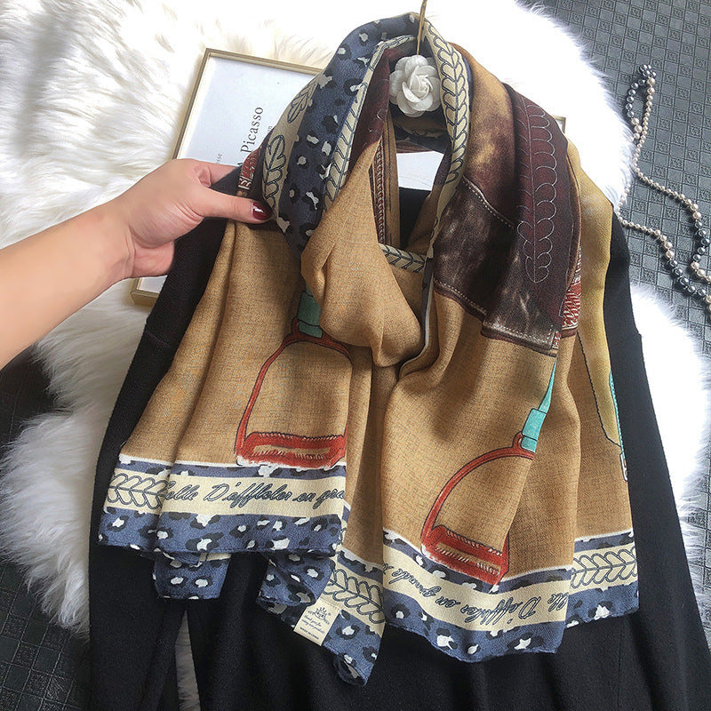Brown scarf with artistic designs held by a hand on a textured surface