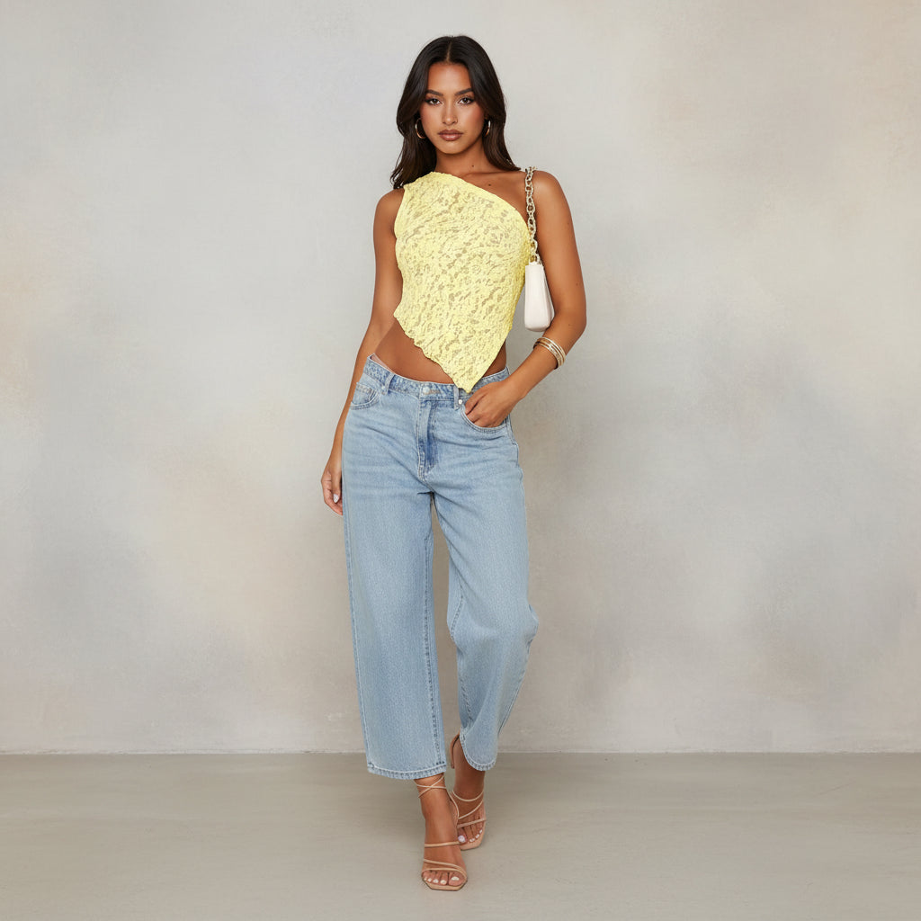 Woman wearing a yellow lace top and blue jeans with a white handbag.