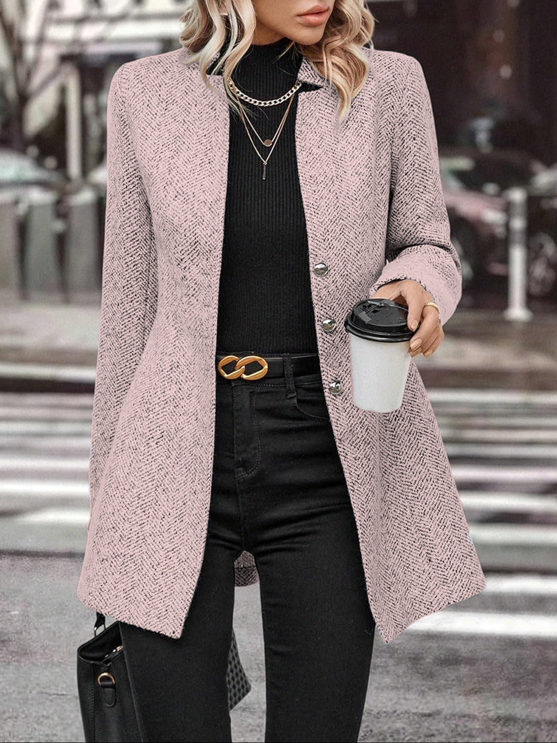 Person wearing a pink coat and black pants, holding a coffee cup on a city street.