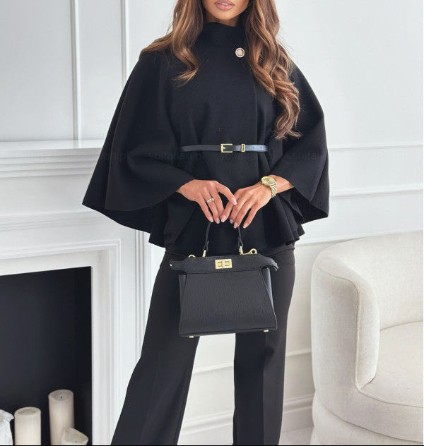 Woman in a black outfit holding a matching handbag in a room with white walls and a fireplace.
