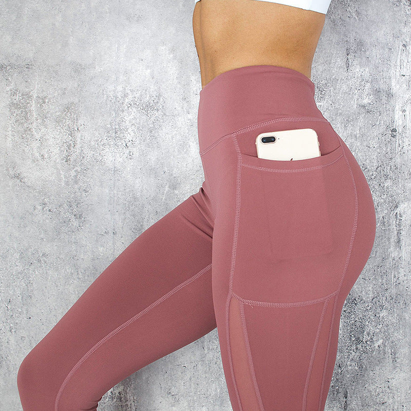 Pink leggings with a pocket holding a phone against a gray concrete wall.
