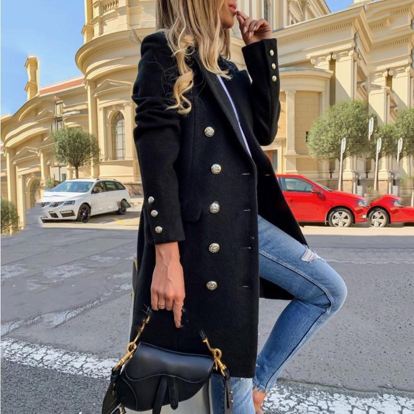 Woman in a black coat with silver buttons and blue jeans standing on a street.