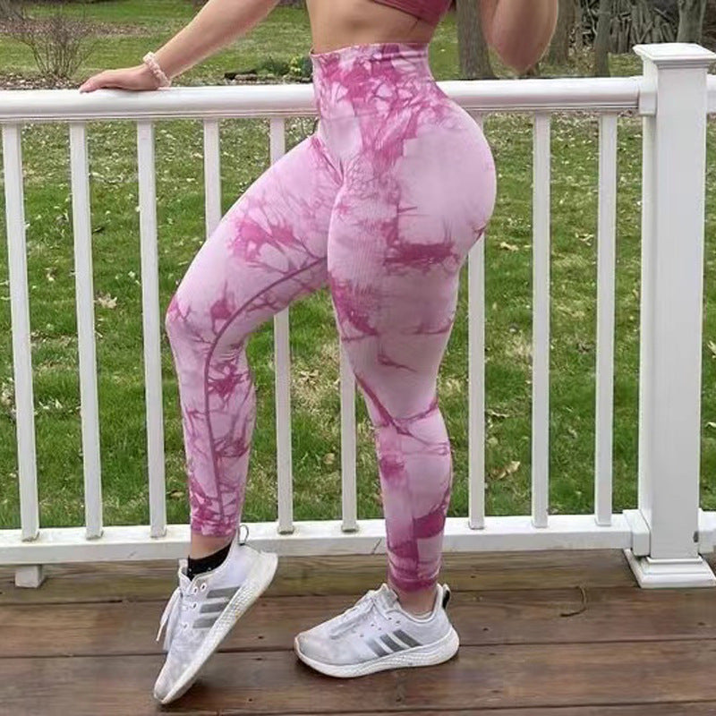 Person wearing pink tie-dye leggings and white sneakers on a wooden deck.