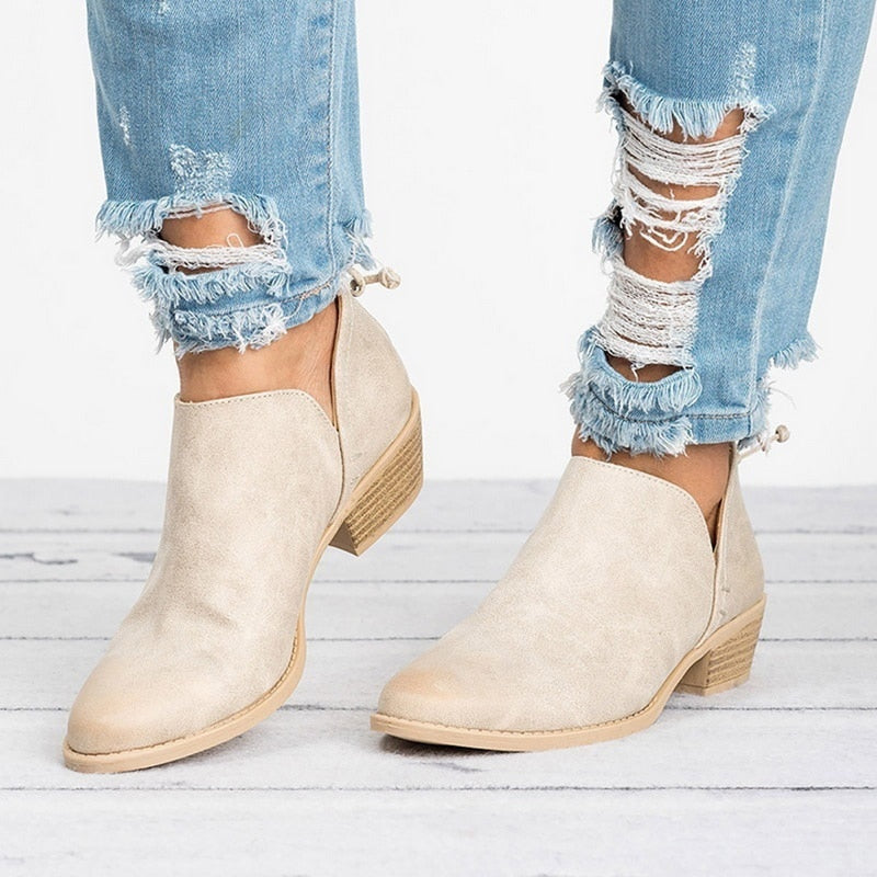 Beige ankle boots worn with ripped jeans on a light wooden floor.