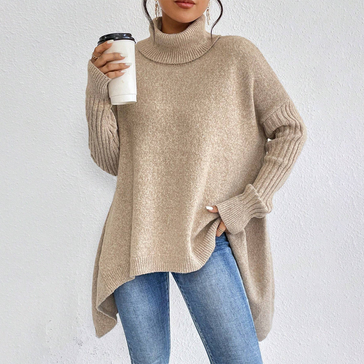 Person wearing a beige sweater and blue jeans, holding a white cup with a black lid.