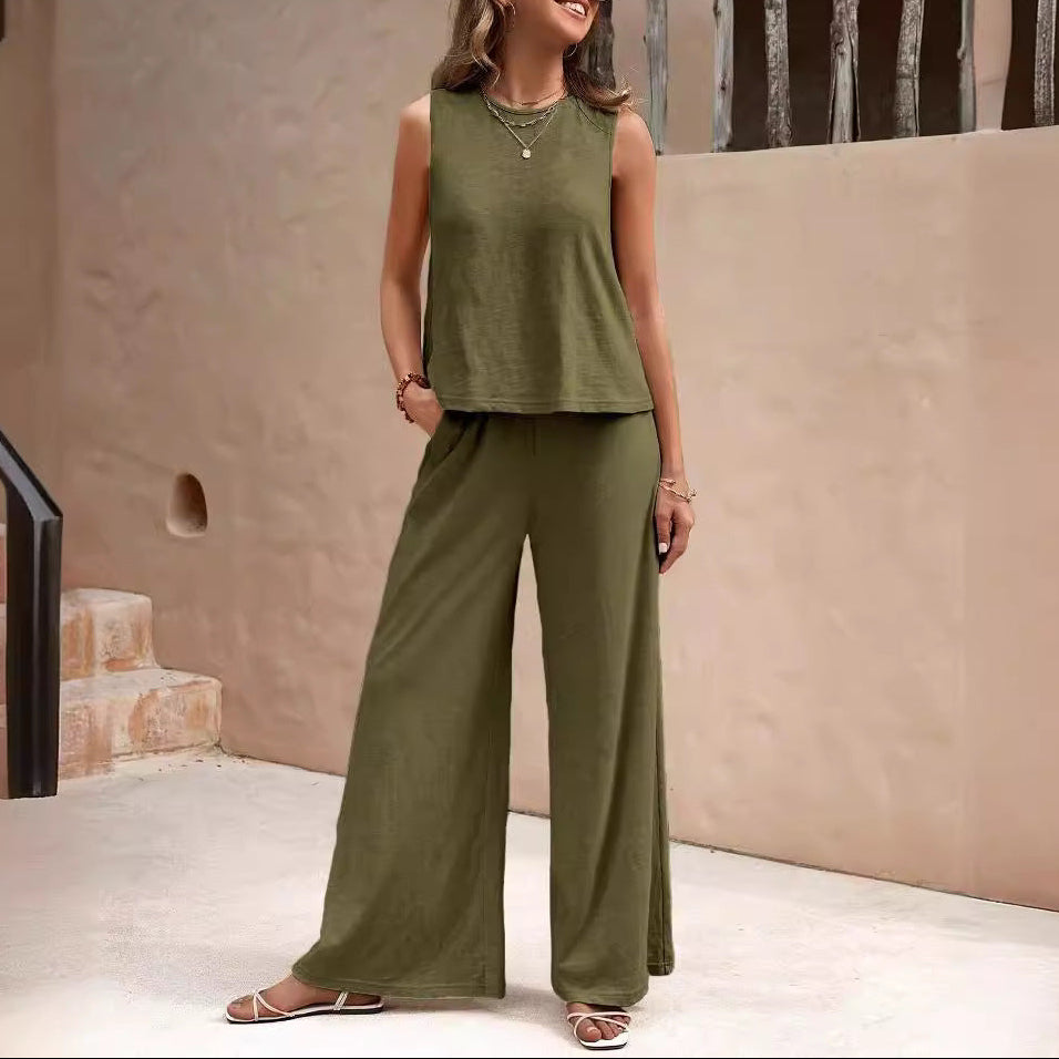 Woman wearing an olive green sleeveless top and wide-leg pants standing against a beige wall.