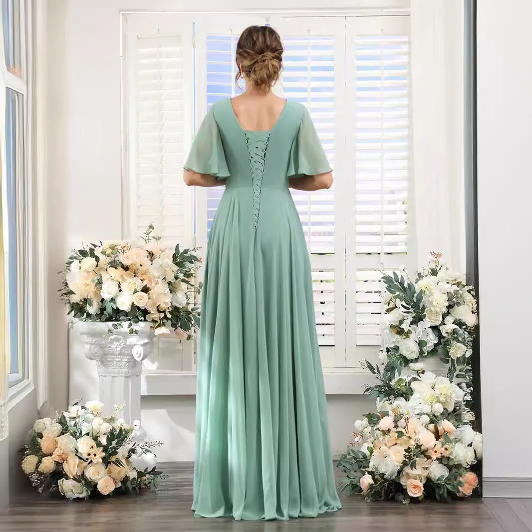 Woman in a long green dress standing in front of floral decorations.