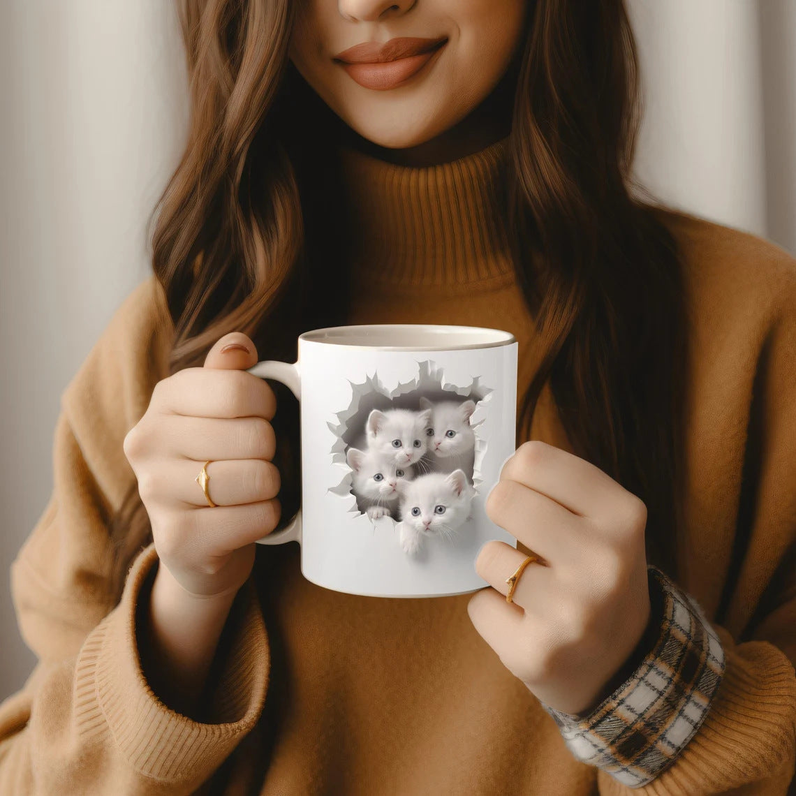 Person holding a mug with a design of three cats, wearing a brown sweater.