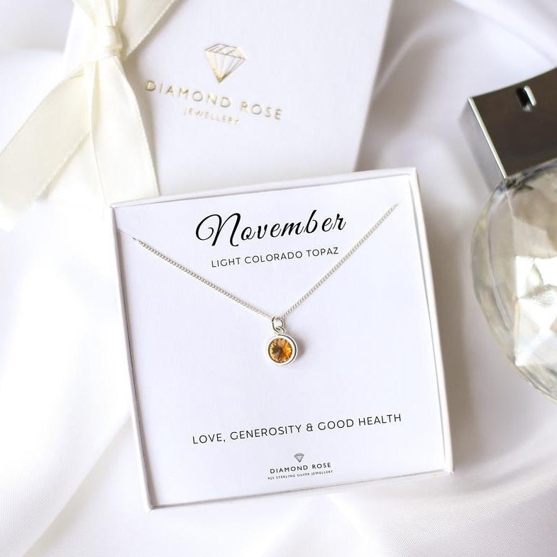 Diamond Rose necklace with light Colorado topaz on a card labeled 'November' with a bottle of perfume in the background.