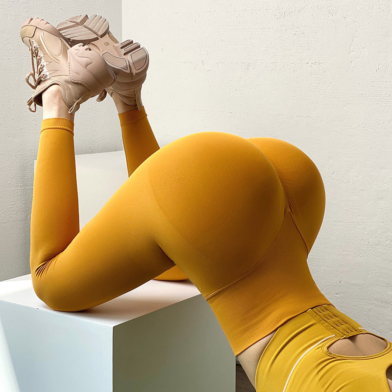 Person wearing mustard yellow leggings and shoes, sitting on a white cube.