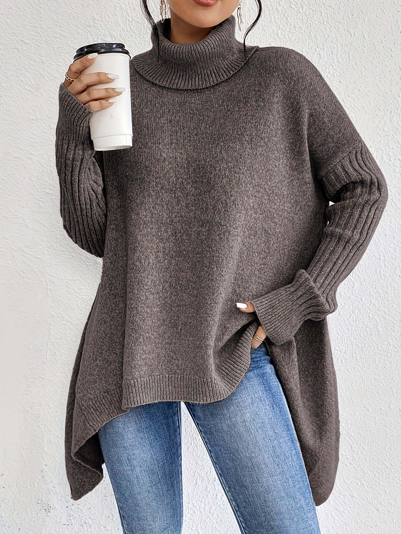 Person wearing a gray sweater holding a white cup against a light background
