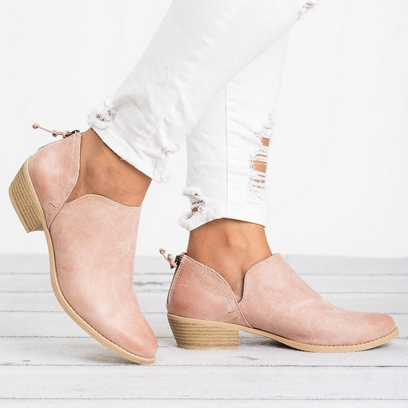 Pink suede ankle boots worn with white distressed jeans on a light wooden floor.