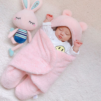 Baby wrapped in a pink blanket with a plush toy next to them on a light background