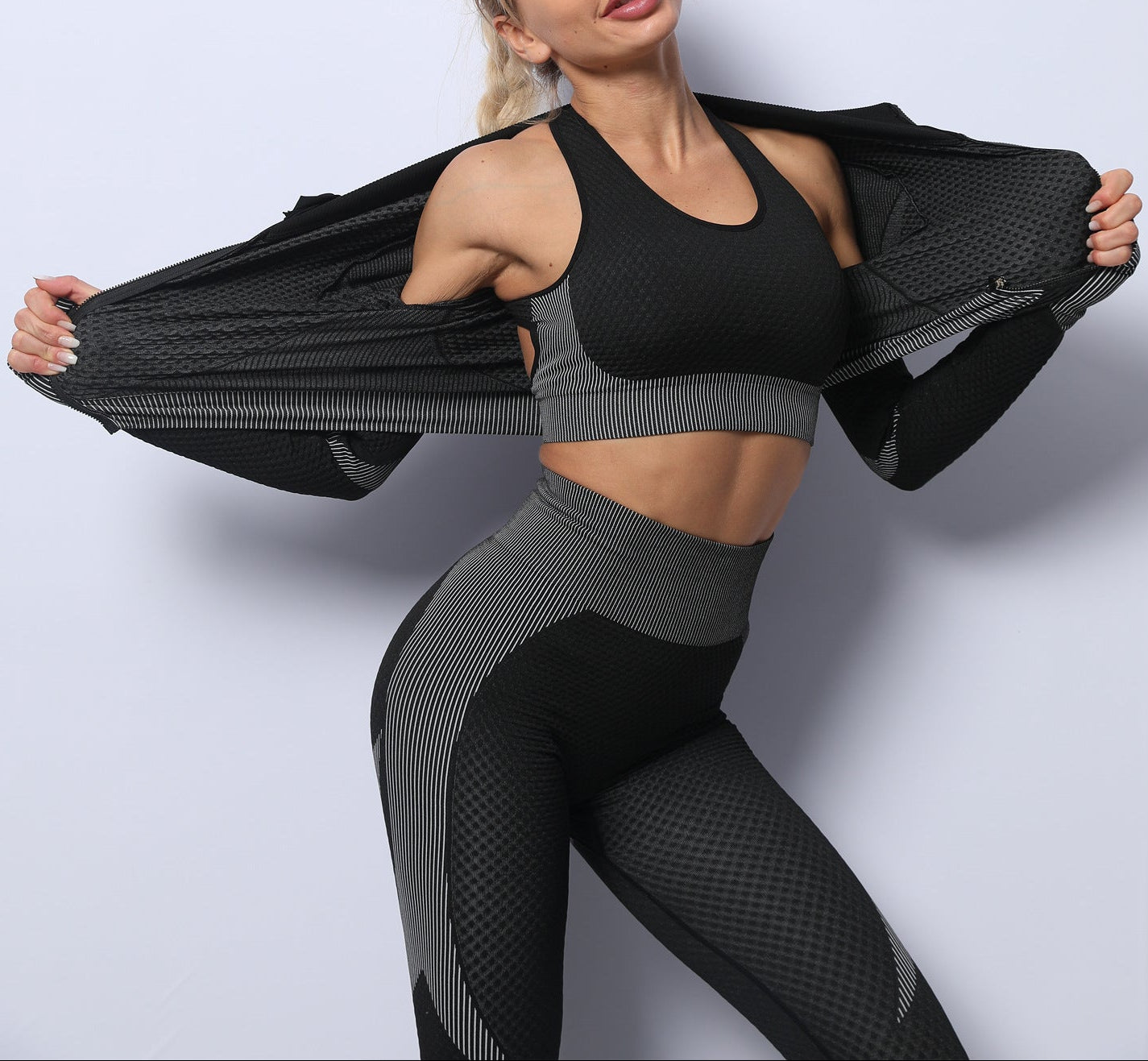 Woman wearing a black sports bra and leggings with a black jacket on a light gray background