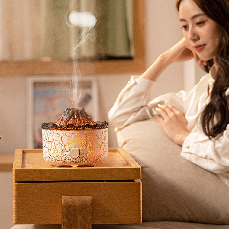 Woman sitting on a couch next to a crackled glass diffuser emitting steam.