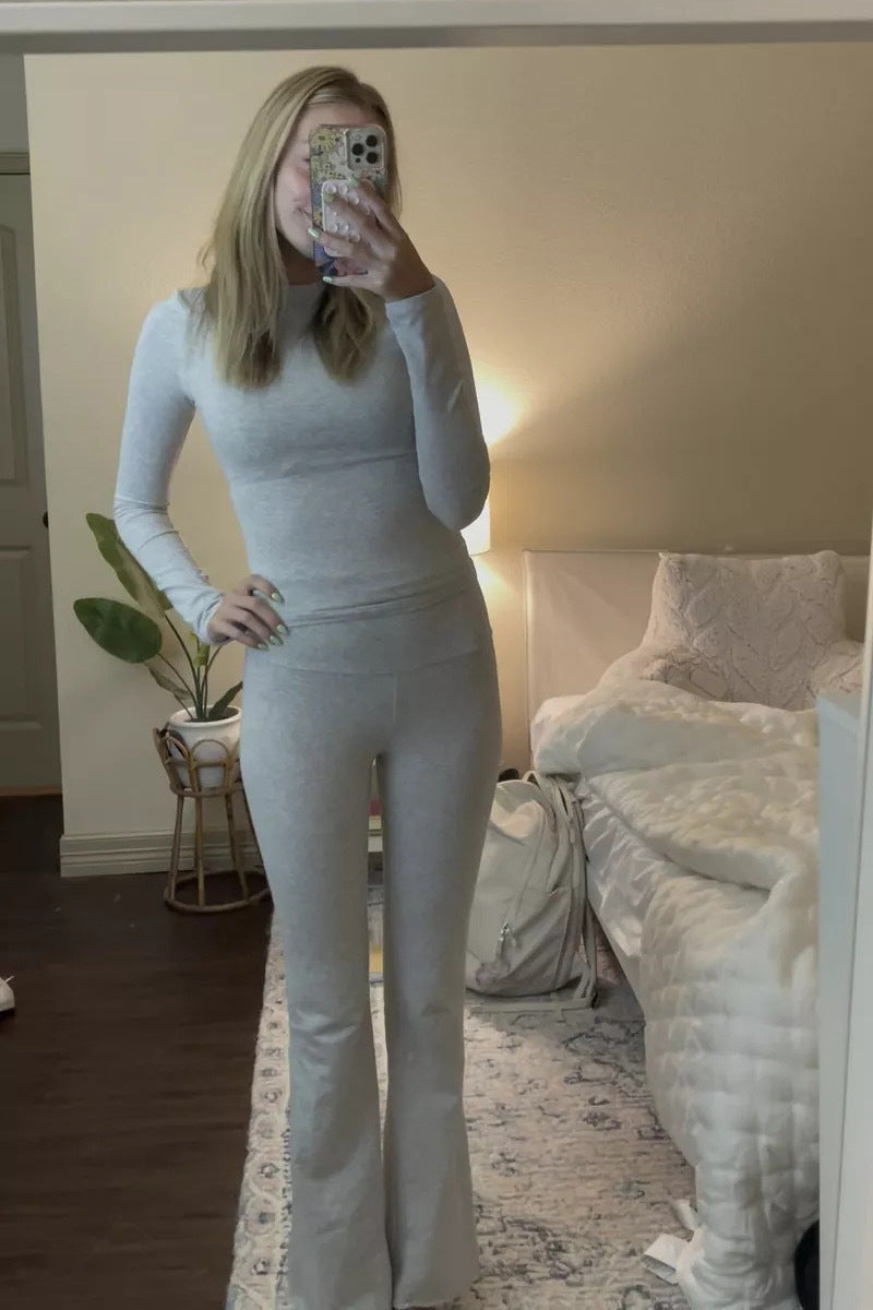 Person wearing a light gray outfit taking a mirror selfie in a bedroom.