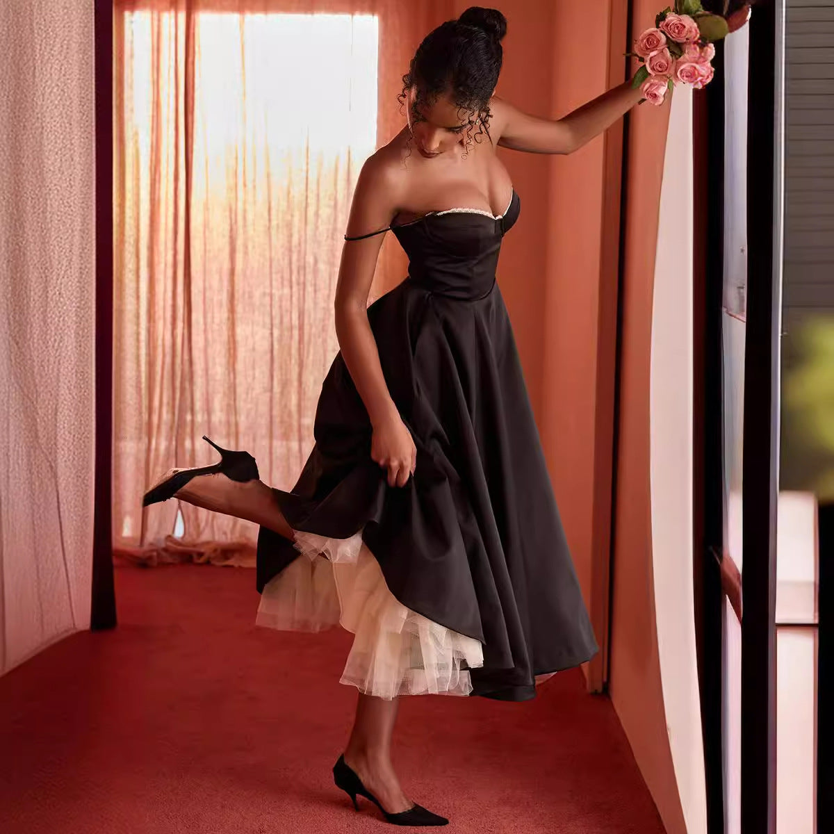Woman in a black dress holding flowers in a room with red carpet and pink walls.