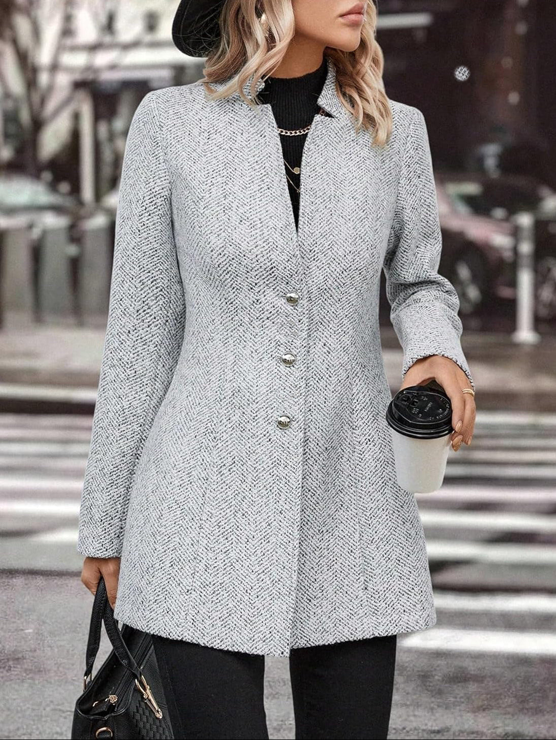 Person wearing a gray coat holding a coffee cup on a city street.