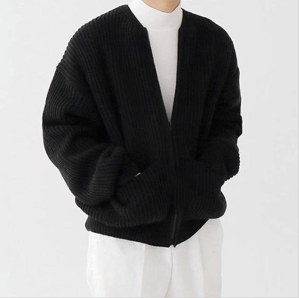 Person wearing a black cardigan over a white shirt and pants on a white background