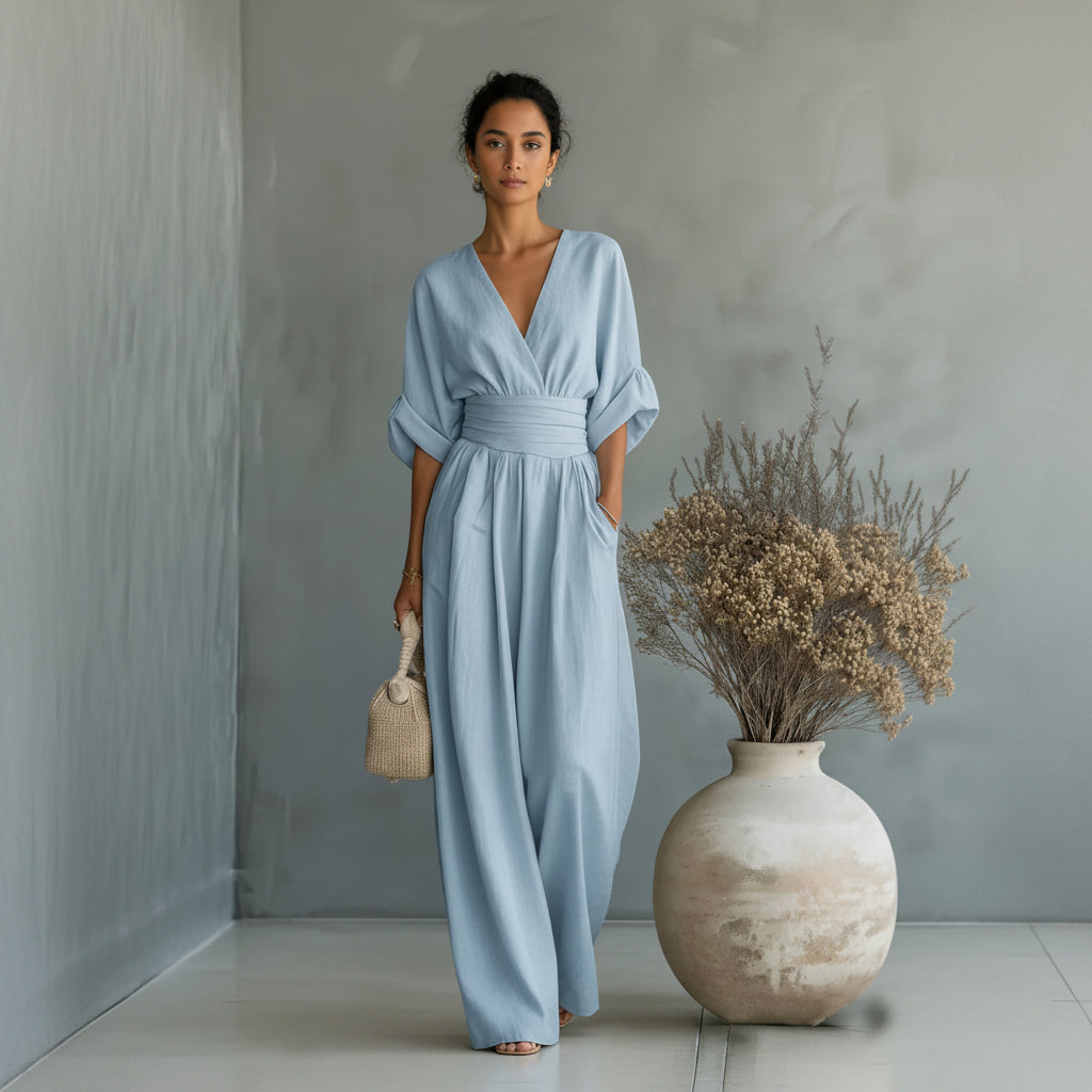 Woman in a light blue dress standing next to a vase with dried flowers against a gray wall.