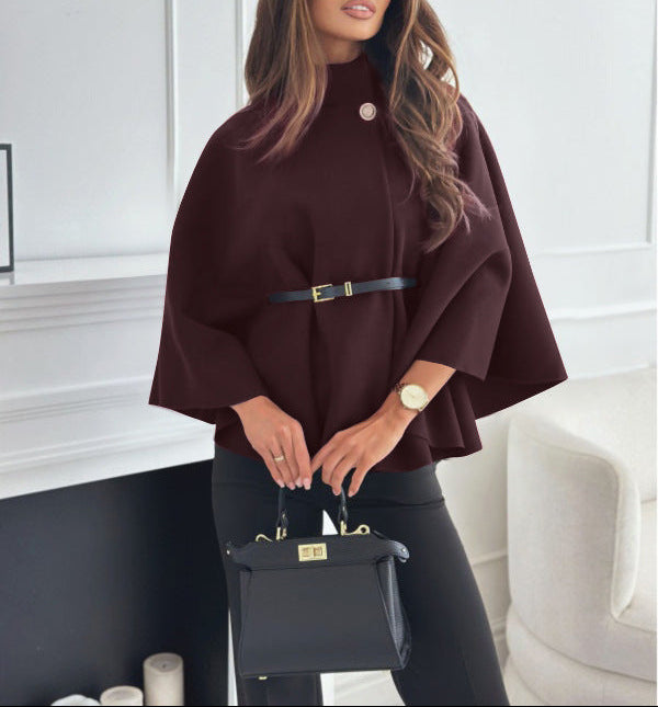 Woman wearing a brown poncho holding a black handbag indoors.
