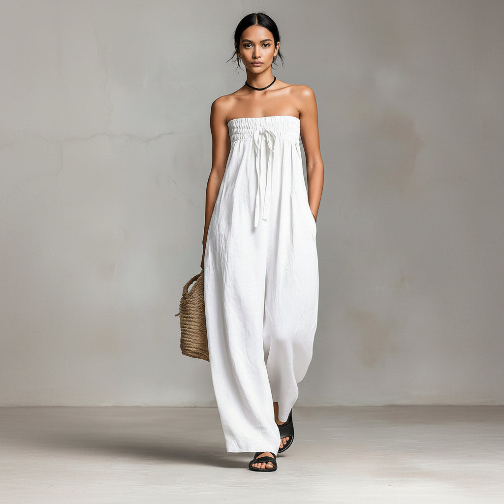 Woman wearing a white strapless dress holding a woven bag against a plain background