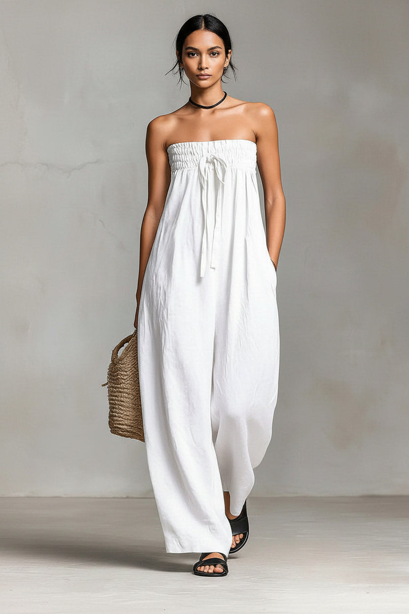 Woman wearing a white strapless dress holding a woven bag against a plain background