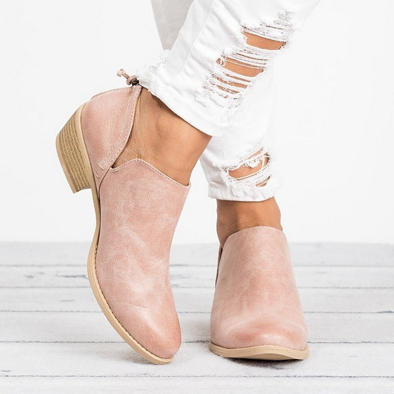 Beige ankle boots worn with white distressed jeans on a light wooden floor.