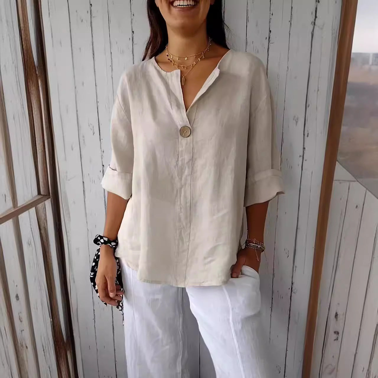 Person wearing a beige shirt and white pants against a wooden wall.