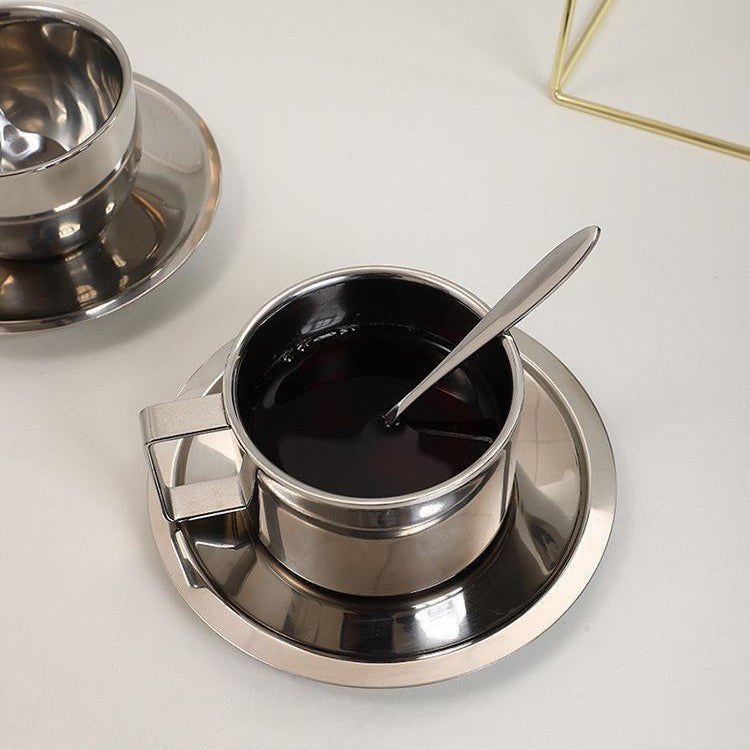 Stainless steel cup with saucer and spoon on a white surface