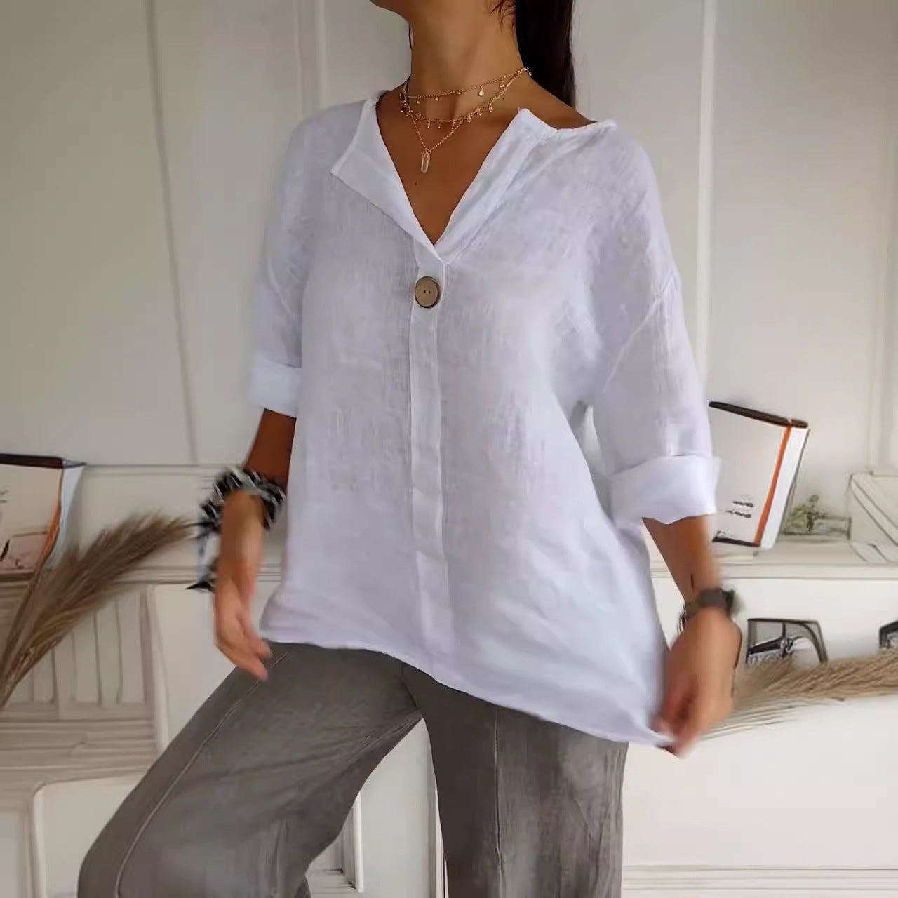Person wearing a white shirt with rolled-up sleeves and gray pants in an indoor setting.