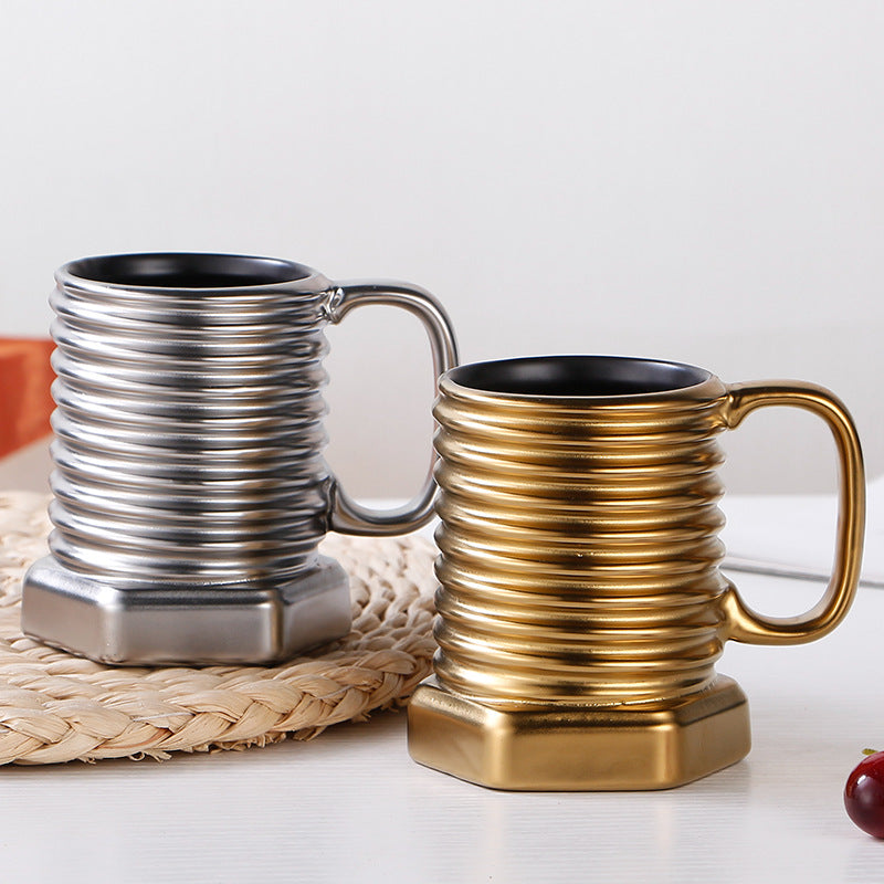 Two metallic mugs, one silver and one gold, on a white surface with a woven mat.