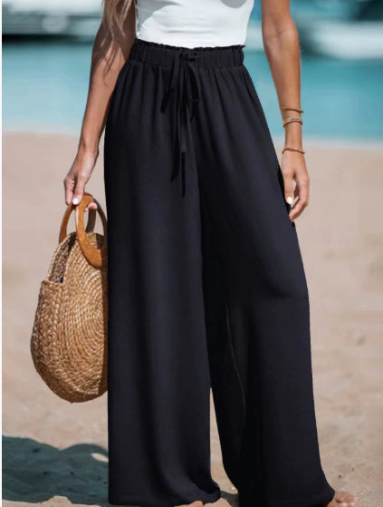 Person wearing black wide-leg pants with a blurred beach background