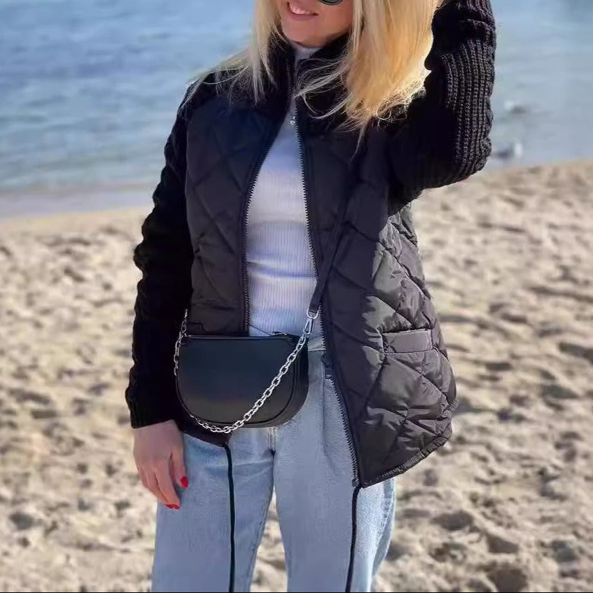 Woman on a beach wearing sunglasses and a black puffer vest with a white top and light blue jeans.