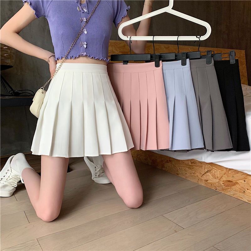 Person wearing a white pleated skirt with other skirts in different colors on hangers.
