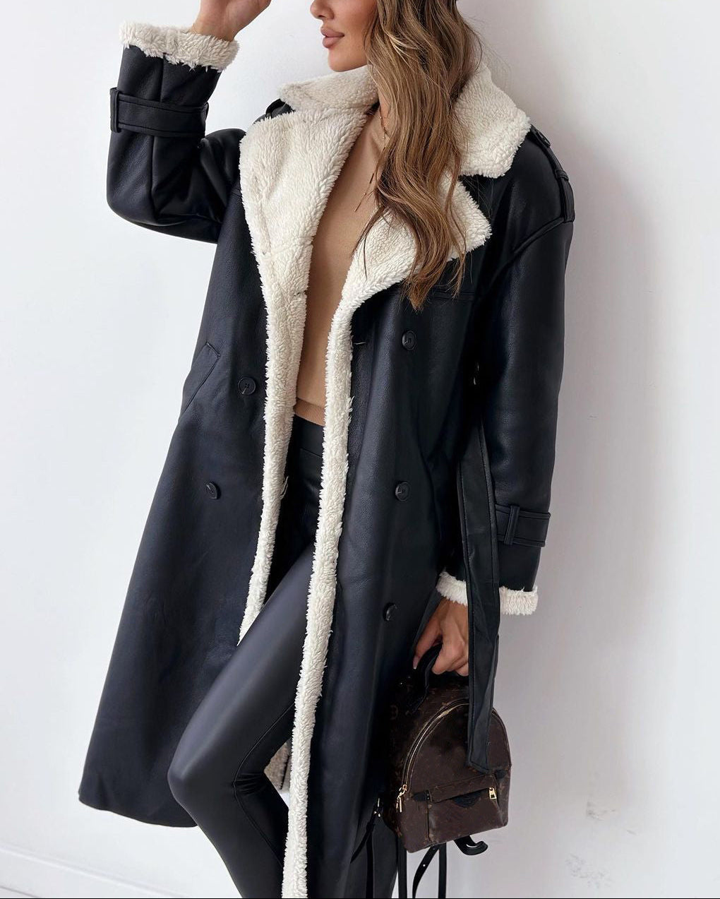 Woman wearing a black coat with white fur lining, holding a brown bag against a white background
