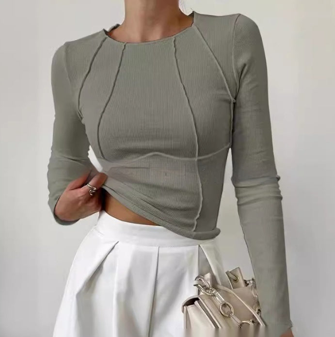 Person wearing a gray long-sleeve top and white pants against a plain background