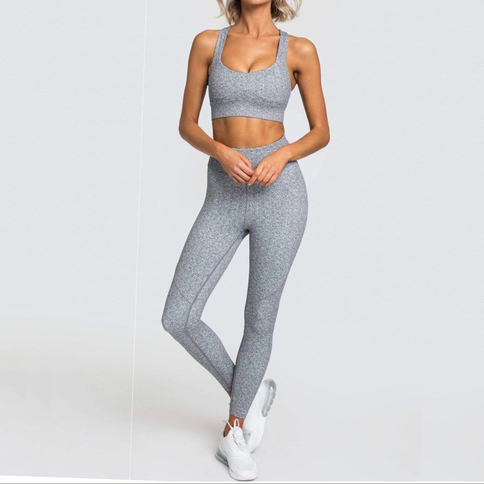 Woman wearing a gray sports bra and leggings set on a white background