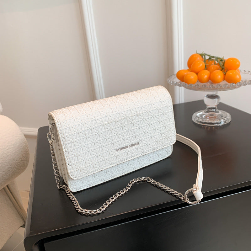 White textured handbag with chain detail on a dark surface, next to a glass dish with oranges.