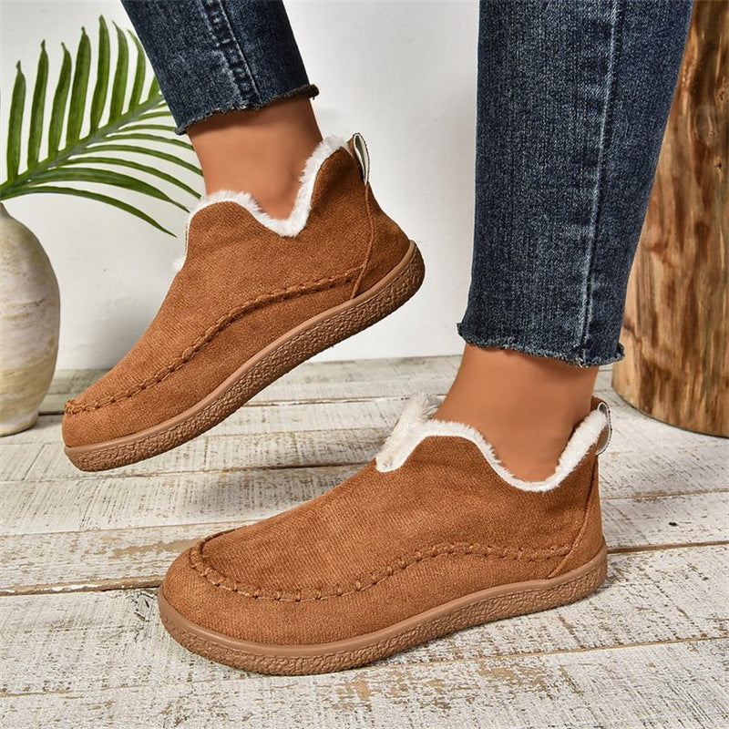 Brown slip-on shoes with white trim worn by a person on a wooden floor.