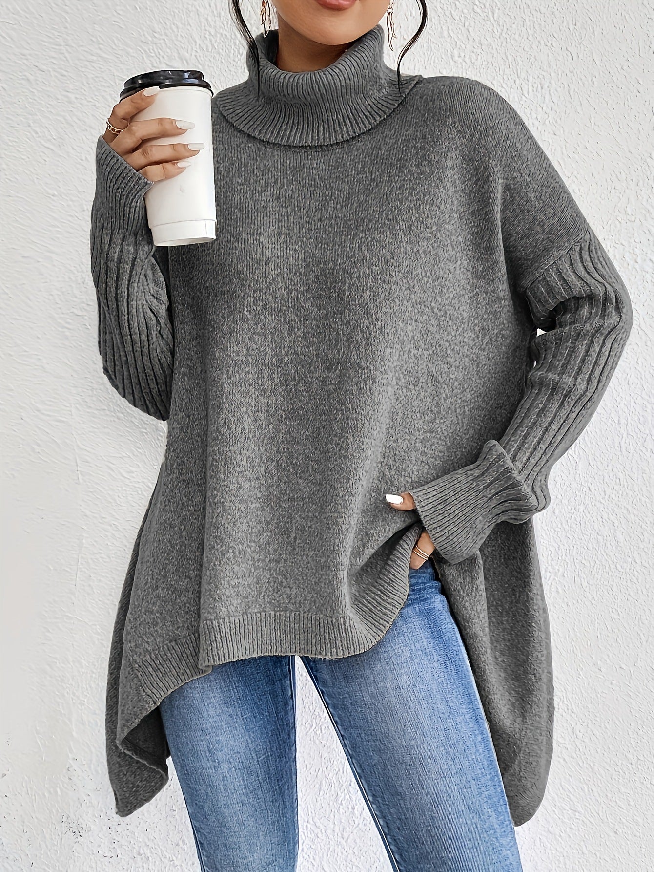 Person wearing a gray sweater and blue jeans holding a white cup against a light background