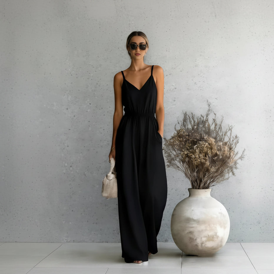 Woman in a black dress standing next to a large vase with dried flowers against a gray wall.