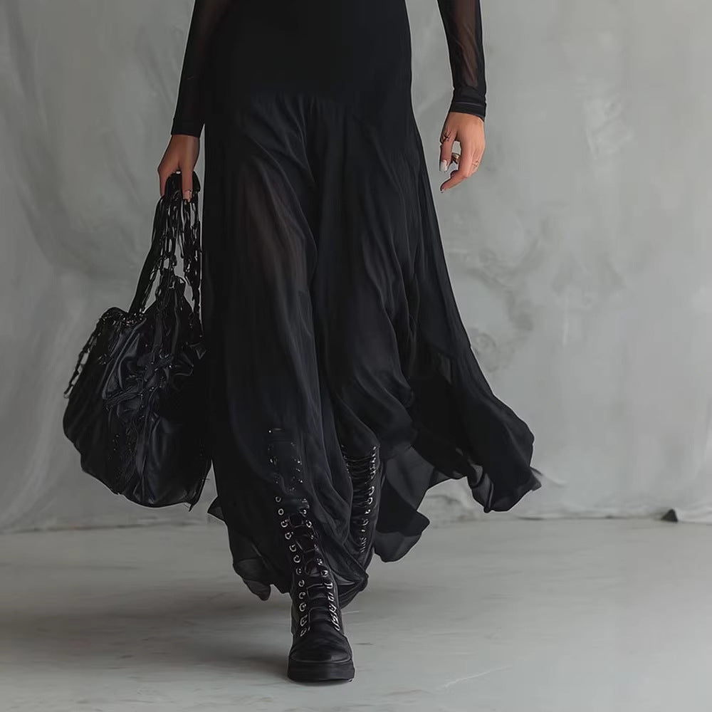 Person wearing a long black dress with sheer sleeves against a gray background