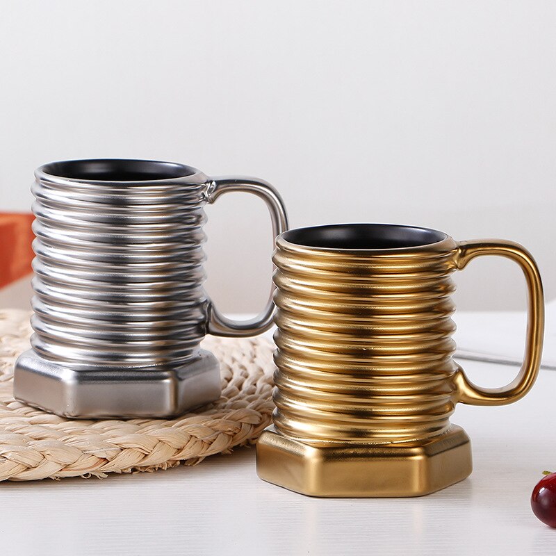 Two metallic mugs, one silver and one gold, on a woven mat with a white background.
