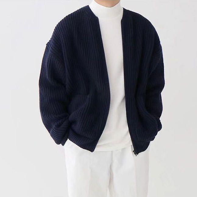 Navy blue cardigan over a white turtleneck and pants on a plain background
